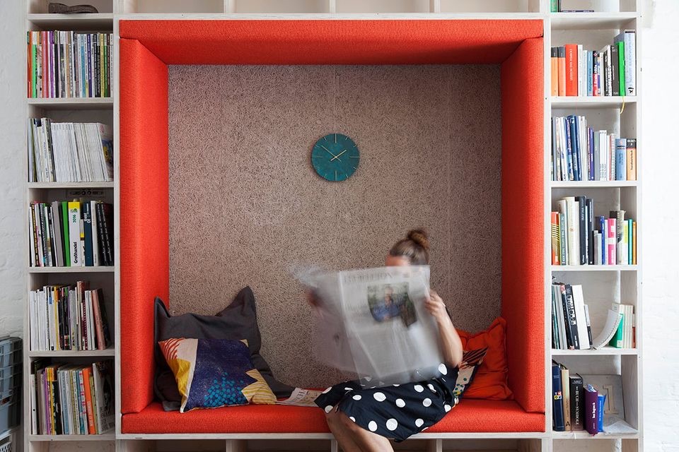 Jessica Kleffner reading a newspaper in a red reading nook between bookshelves